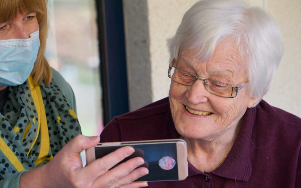 Elder care provider shares smartphone screen with elderly resident.