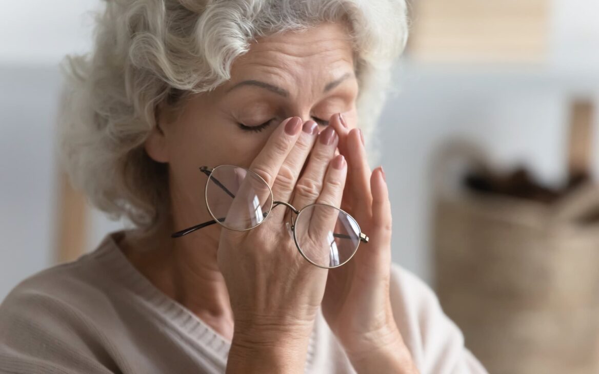 Elderly women presses her hands against the sides of her nose in stress.