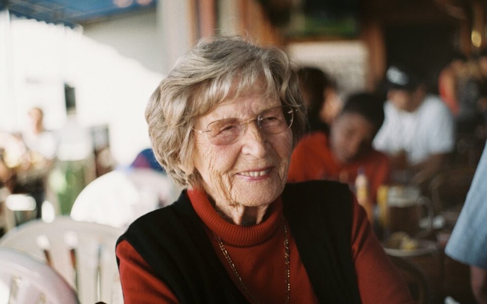 An elderly woman smiles while dining at a restaurant.