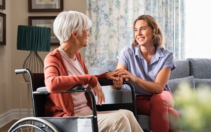 Smiling adult woman sits next to an elderly woman in a wheelchair.