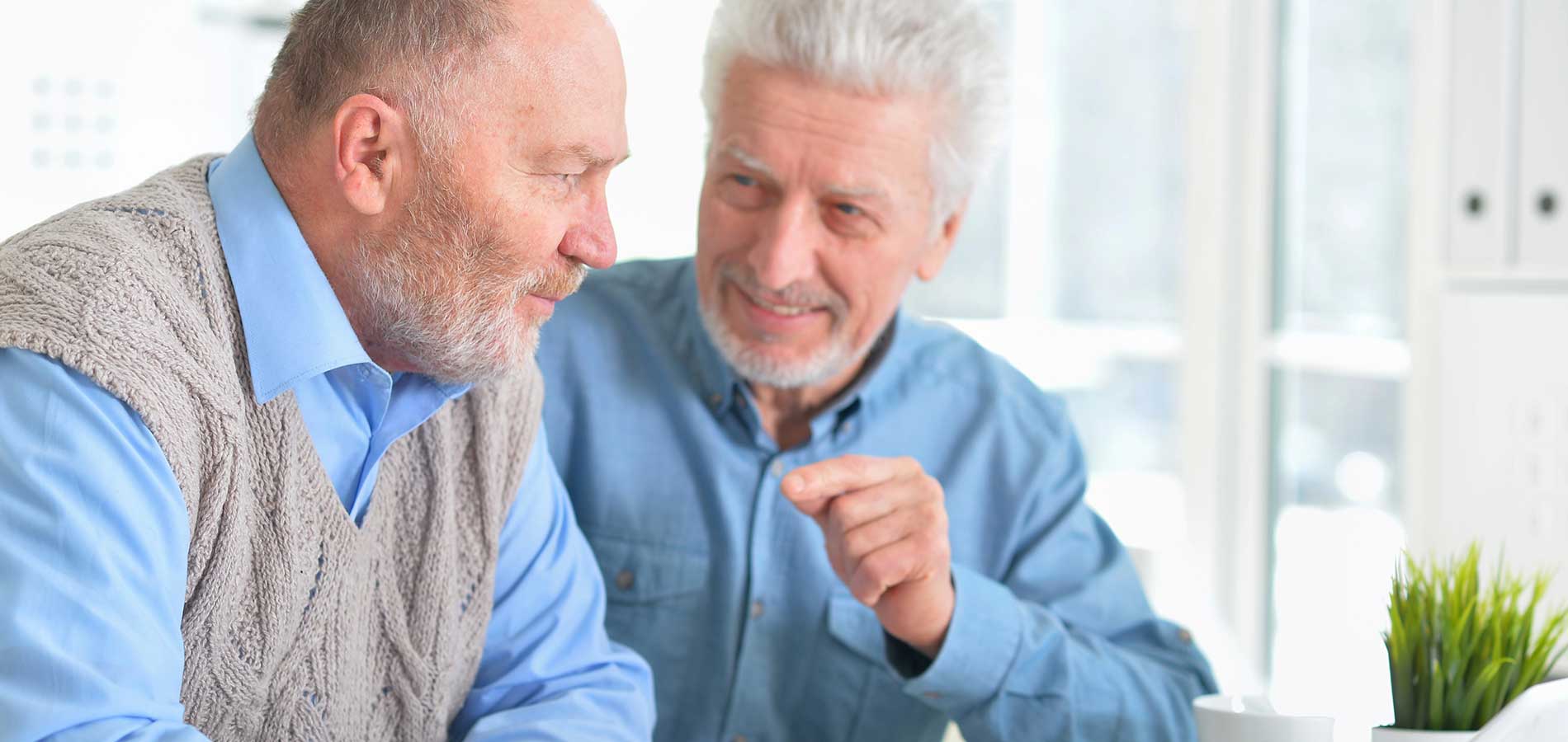 Two senior men smiling and conversing in a bright kitchen setting.