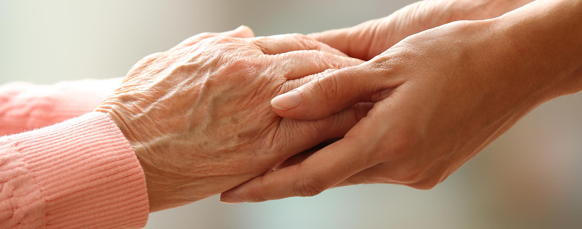 Two hands holding, one from an older person with visible wrinkles and one from a younger person, symbolizing care and support.