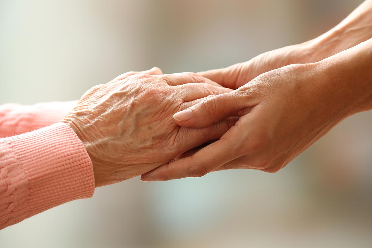 Two hands, one with visible signs of aging, gently holding each other, symbolizing care and support.